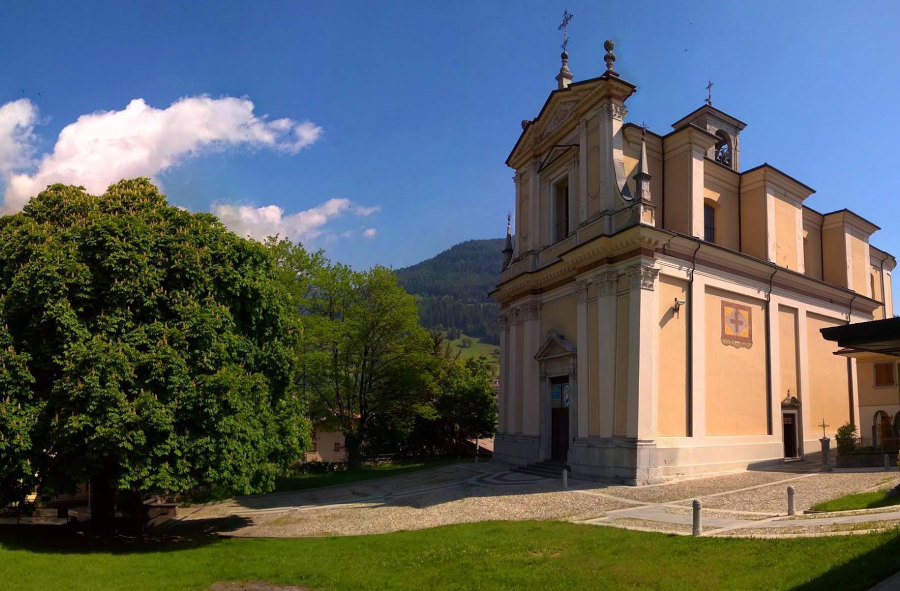 PARROCCHIALE CON A SINISTRA IL CENTENARIO IPPOCASTANO - Prima dell'attuale edificio cristiano settecentesco, delicato a S. Giovanni Battista, si sa dell'esistenza in Borno di due primitive cappelle. Da un documento del 1018 si ha notizia che sul medesimo dosso ove sorge attualmente la chiesa parrocchiale, esisteva una cappella dedicata a S. Martino di Tours. Più tardi, sulla stessa area, ne fu edificata una seconda, consacrata dal vescovo bresciano Maifredo nell'anno 1146. Quest'ultima ebbe doppio titolo consacratorio, all'antico titolo di S. Martino fu aggiunto quello di S. Giovanni Battista. La seconda cappella fu parziamente demolita e riedificata nell'anno 1449. (...) Fu  soltanto alla fine del 1700, che si abbandonò l'idea dei continui rimaneggiamenti per abbbracciare quella della ricostruzione "ex novo". La chiesa nuova, quella attuale, fu iniziata nella primavera del 1771 su progetto del milanese Pier Antonio Ceti, e fu ultimata soltanto nel 1781, dieci anni dopo (non undici, perchè nel 1775, anno santo, non si lavorò)... Il complesso architettonico si presenta fra quelli più armonici della Valcamonica, la sua euritmia scaturisce dall'esatta proporzione e dalla giusta disposizione delle parti. Un ampio sagrato che sovrasta la piazza Umberto 1°, servito da gradinata, da accesso al portale d'ingresso.  (Da "Borno e la sua storia", di G. Goldaniga)