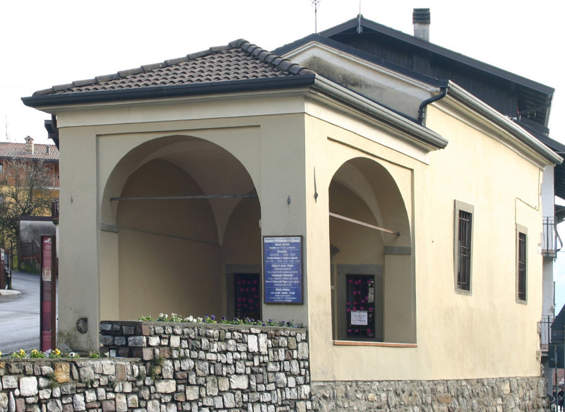 CHIESETTA DELLA DASSA dedicata all'apparizione della Madonna a Lourdes - All'uscita dell'antico nucleo abitato, sul lato destro di Via Vittorio Veneto, un tempo denominata strada comunale della Dassa, sorge una modesta cappella consacrata alla Madonna di Lourdes. Fu eretta probabilmente intorno al 1500. L'ultima e forse più consistente opera di restauro, apportata nell'anno 1917, ha evidenziato l'attuale struttura. Anticamente era dedicata ai Santi Vito e Modesto, ancor oggi affrescati sulle pareti interne della pieve (lato destro). In una nicchia incavata sopra l'altare è riprodotta in miniatura la grotta e la statua della Madonna di Lourdes. All'esterno, sulla facciata principale d'ingresso vi è addossato un porticato che evidenzia sui lati occidentale e meridionale archi a pieno centro sostenuti da pilastri. Data la modesta dimensione dell'edificio, l'interno è a navata unica. La volta a crocera della medesima presenta affrescature di rilievo che la occupano per intero. Si tratta della raffigurazione dell'incendio di Borno, probabile opera (quantomeno restaurata) dal pittore bornese Enrico Peci. (Da "Borno e la sua storia", di G. Goldaniga) - vedi articolo